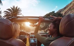 Travel people having fun driving in trendy convertible car in a tropical city. 