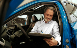 Man sitting in a car in a car dealership writing something down on a clipboard