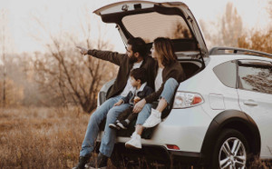 Famille assise à l'arrière de leur voiture à hayon et pointant le doigt au dehors. 