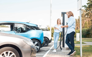 Young adult friends talking and charging electric car