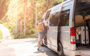 Passenger boarding on travel van with carry bag and bottle water.