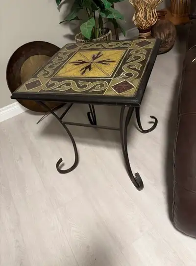 This end table features a decorative top with intricate tile work. It has a dark metal frame with sc...