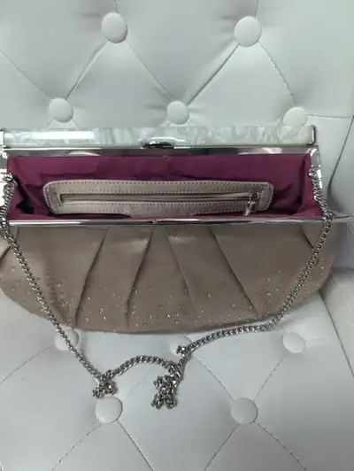 This clutch has a silver chain strap, a white, semi-transparent clasp, and a pink lining. It has a z...
