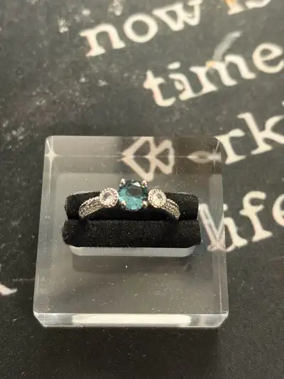 This is a lovely three-stone ring in good pre-owned condition featuring a stunning teal-coloured cen...