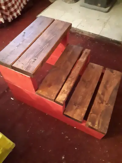 This is a hand-crafted step stool with a vibrant red base and stained steps, perfect for adding a to...
