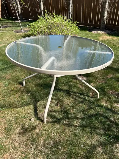 Round patio table 4’ wide x 28” high. Glass top with a hole for an umbrella. The metal frame is stur...