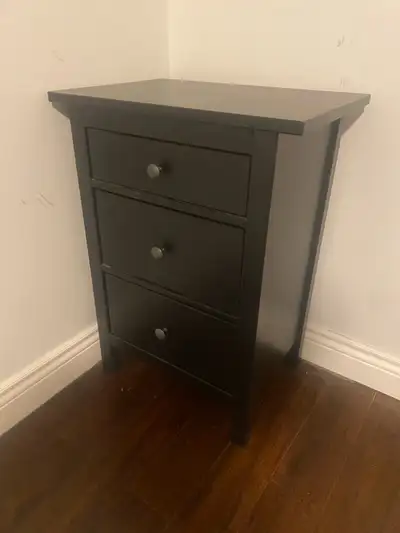 This is a black IKEA nightstand with three drawers, perfect for adding storage and style to your bed...