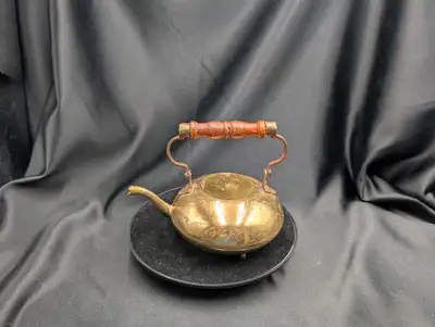 A vintage brass teapot. Features include a rounded or pot-belly shape, a swan-neck spout, and a wood...