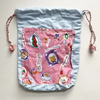 This handmade blue and pink drawstring bag features a cute print of doodles varying from a bear, tul...