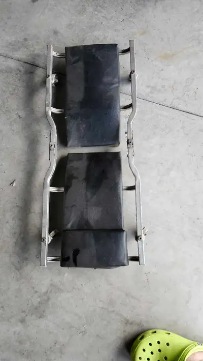 This is a used mechanic's creeper, featuring a sturdy metal frame and two padded black vinyl support...