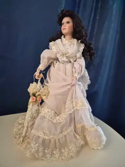 This is a used Heritage Signature Collection porcelain doll with dark curly hair, dressed in an eleg...
