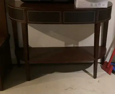 This is a console table with a rich, dark wood finish and faux-leather drawer fronts, adorned with d...