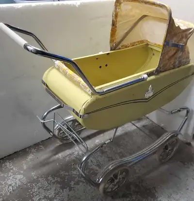 A classic 1960s vintage baby pram with a yellow exterior and a floral interior lining. It has a chro...