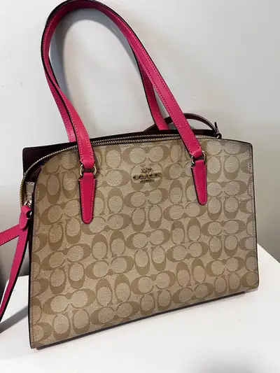 Stylish Coach shoulder bag with signature pattern. Tan body with striking pink handles. Perfect for...