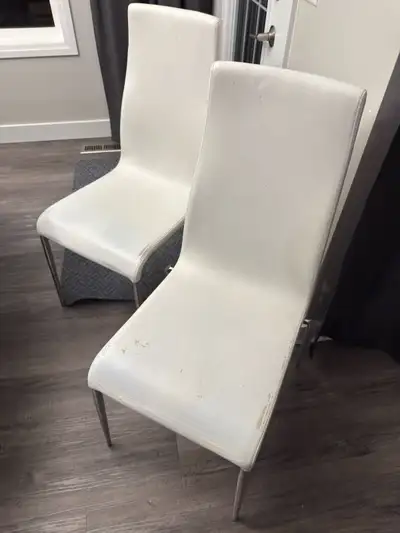 These are a set of five modern dining chairs, featuring a sleek design with white faux-leather seats...