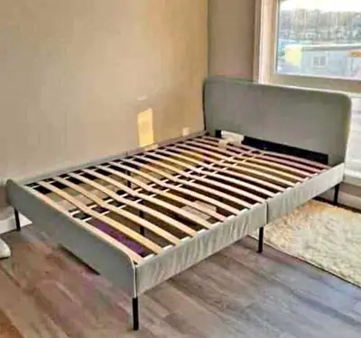 This is a queen bed frame with a light grey upholstered headboard and black metal legs, offering a m...