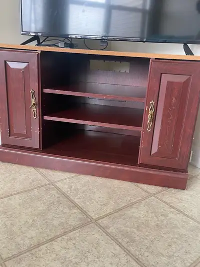 This is a dark red wood tv stand with two doors for storage and interior shelving. It's a functional...