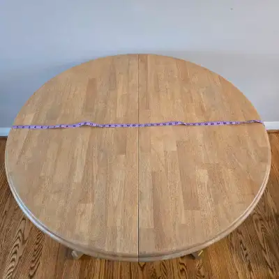 This is a used round dining table with a pedestal base and a leaf that extends it into an oval shape...
