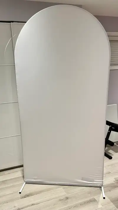 This elegant white arched backdrop stand features a sleek, minimalist metal frame with a fitted fabr...