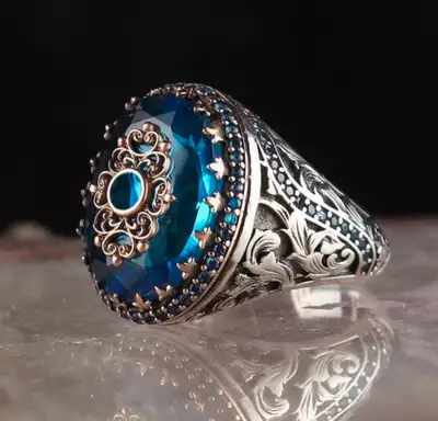 This eye-catching ring features a large, oval-cut blue gemstone, possibly a blue topaz or sapphire s...