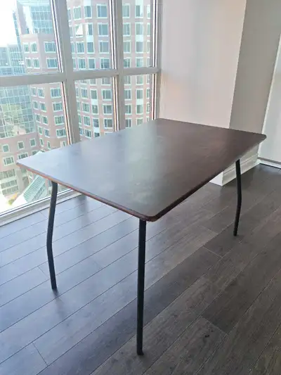 This sturdy folding dining table features a rectangular wood-finish top with sleek, black metal legs...