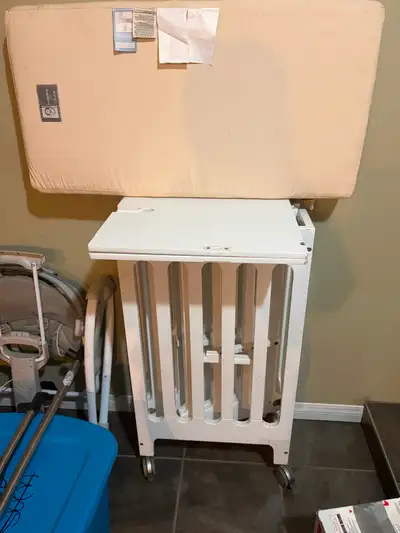 Alma Bloom mini crib with mattress, in white. This crib has wheels that can be locked into place or...
