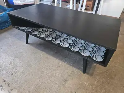 This coffee table features a sleek black finish and a stylish shelf with a patterned design, perfect...