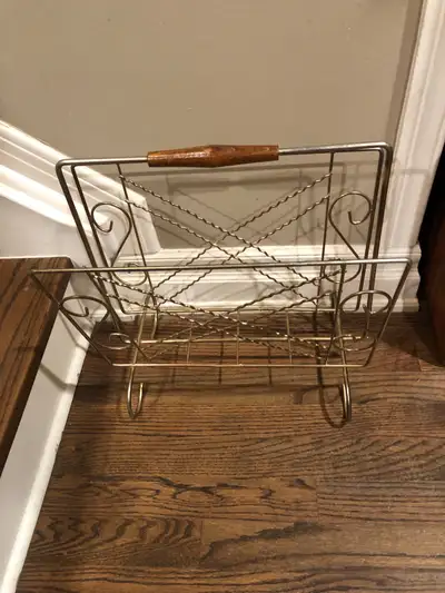 This vintage magazine rack features a gold-tone metal frame with a wooden handle, perfect for adding...