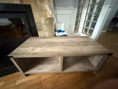 Voici une table basse robuste et d'occasion, avec une finition rustique imitation bois, parfaite pou...