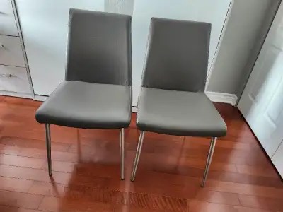 Deux chaises de salle à manger ou cuisine, en cuir gris, pattes en métal brossé. Très confortables.