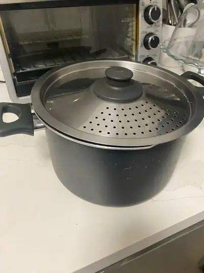Large black stock pot. Features a perforated stainless steel steamer lid. Used condition, shows some...