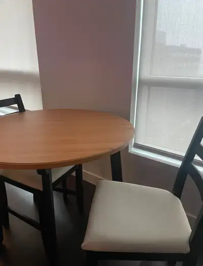 Small round table with two chairs. Light wood top, black legs. Off-white cushioned seats. Good for s...