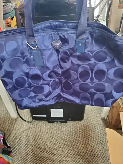 A stylish Coach tote bag in a deep navy colour. It features the signature 'C' pattern throughout the...
