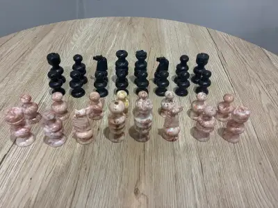 This is a 32-piece chess set crafted from stone, featuring distinct black and tan/white pieces in a...