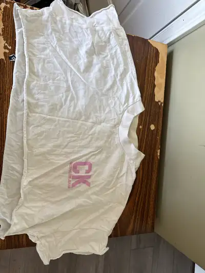Off-white cropped t-shirt. Features a pale pink CK logo. Short sleeves. Slightly oversized fit.