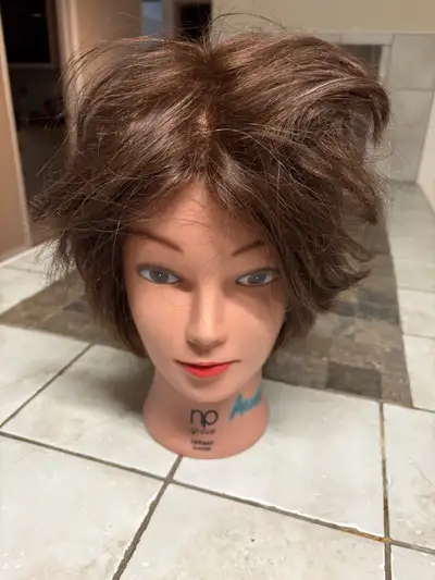 This cosmetology mannequin head features short, layered brown hair, perfect for practicing various s...
