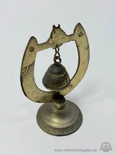 Small decorative brass bell mounted within a horseshoe shaped metal frame on a round weighted base....