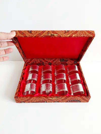 12 silver toned napkin rings in a batik-patterned box, View more