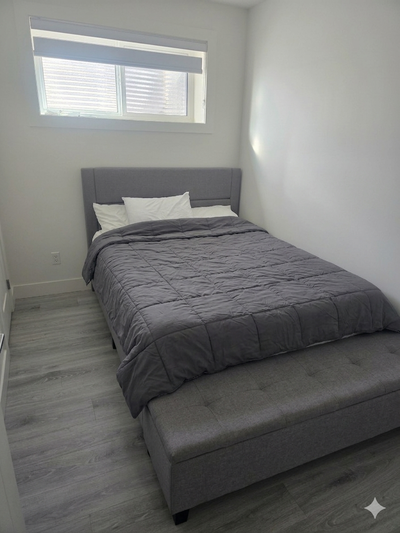 Upholstered queen-sized bed frame in grey fabric. It has a padded headboard with horizontal stitchin...
