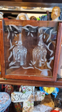2  NEW CRYSYAL WINE GLASSES HANGING IN A WOODEN CABINET