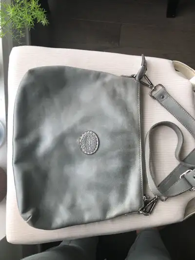 This is a Roots grey leather purse, perfect for everyday use with its comfortable crossbody strap. A...