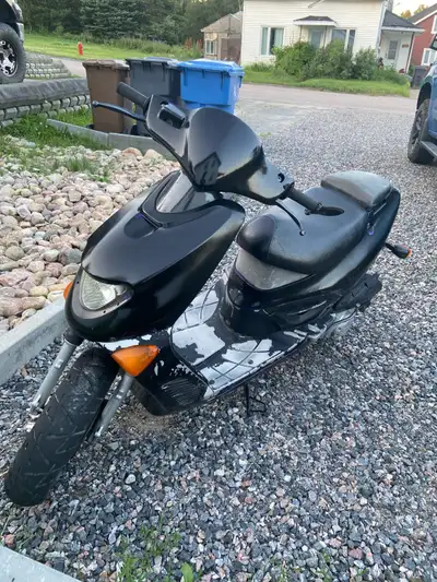 Un scooter noir avec deux pneu de rechange un bac de piece pi un autre scooter bleu . De plus le sco...