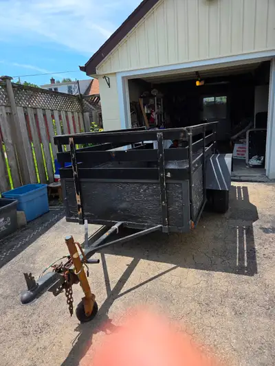 Sturdy utility trailer has a wooden body with high slatted sides. The frame is made of black painted...