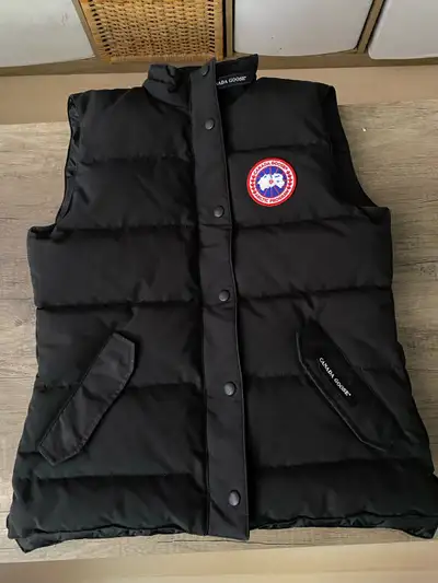 Black Canada Goose vest with a zipper and button closure. Made in Canada with domestic and imported...