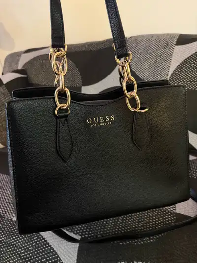 Black Guess tote bag with gold-tone chain detailing on the straps. The bag features the "GUESS LOS A...