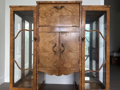 This antique liquor cabinet features intricate woodwork and glass display shelves, perfect for showc...