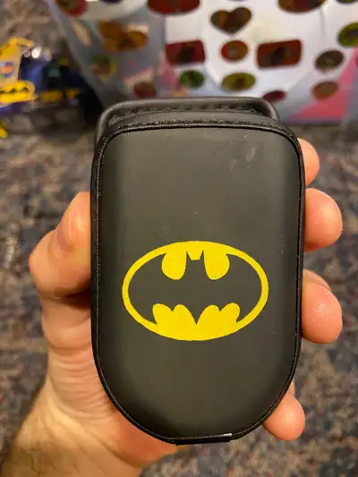 Black carrying case. Features a yellow Batman logo. Small size. Elastic band closure. From the 2000s...