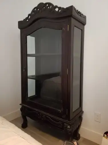 This curio cabinet features a dark wood finish, glass doors and sides, and ornate carvings on the le...