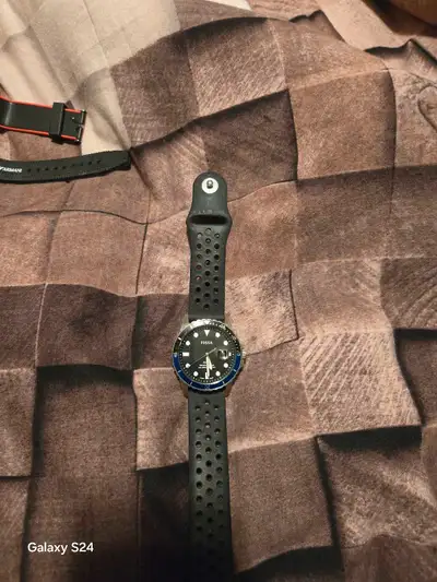 This is a used Fossil watch with a blue bezel and a black silicone strap, perfect for everyday wear....