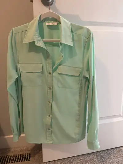 This is a stylish mint green Calvin Klein shirt in a size S. It features two front pockets and a but...